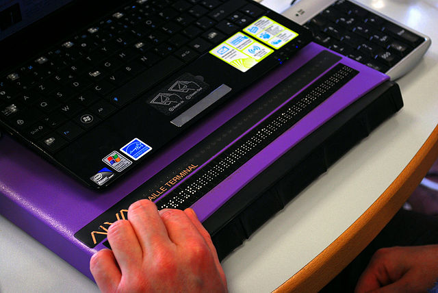 Photo d’une main posée sur un afficheur braille éphémère relié au clavier d’un ordinateur portable