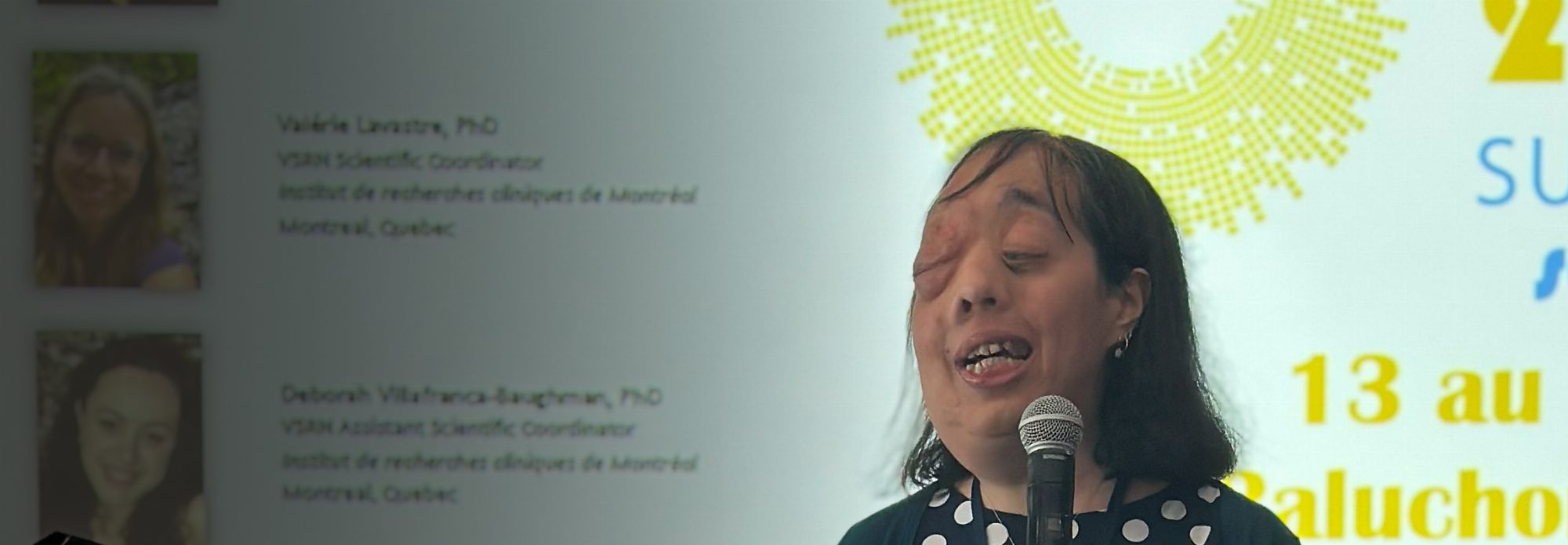 Natalina Martiniello parle au micro à l’avant d’une salle de conférence, devant une diapositive projetée de l’école d’été 2026 du Réseau de recherche en sciences de la vision.